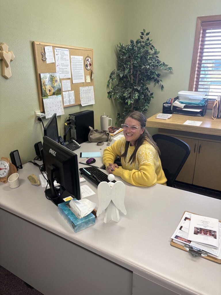 A smiling woman sits at a desk in her office.